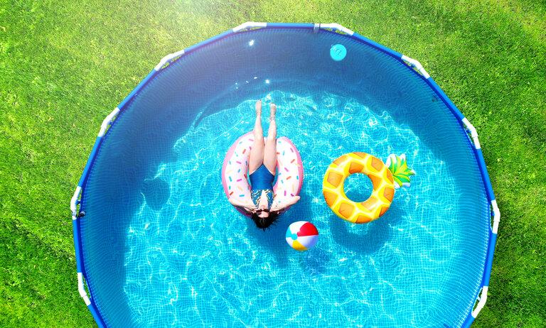 Luftaufnahme. Mädchen ruht in einem Metallrahmen Pool mit aufblasbarem Spielzeug. Sommer Freizeit und Spaß Konzept. Frame Pool stehen auf einem grünen Rasen. Draufsicht von einer Drohne.