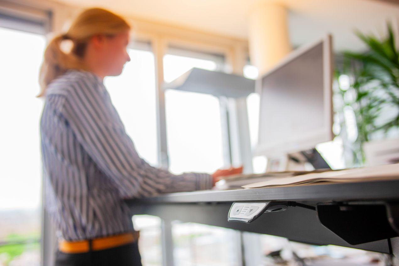 Eine Frau arbeitet an einem höhenverstellbaren Schreibtisch und zeigt, wie ergonomische Maßnahmen Teil der betrieblichen Gesundheitsförderung sind.