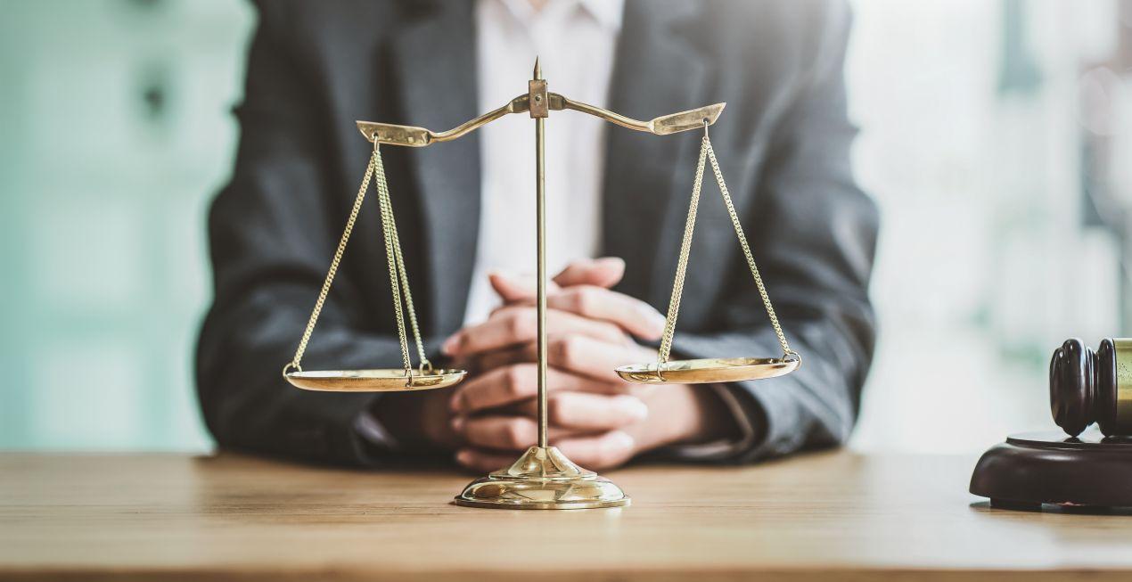 Goldene Waage der Gerechtigkeit auf einem Schreibtisch, im Hintergrund ein Anwalt – Fachanwalt für Strafrecht in Neuss berät Mandanten.