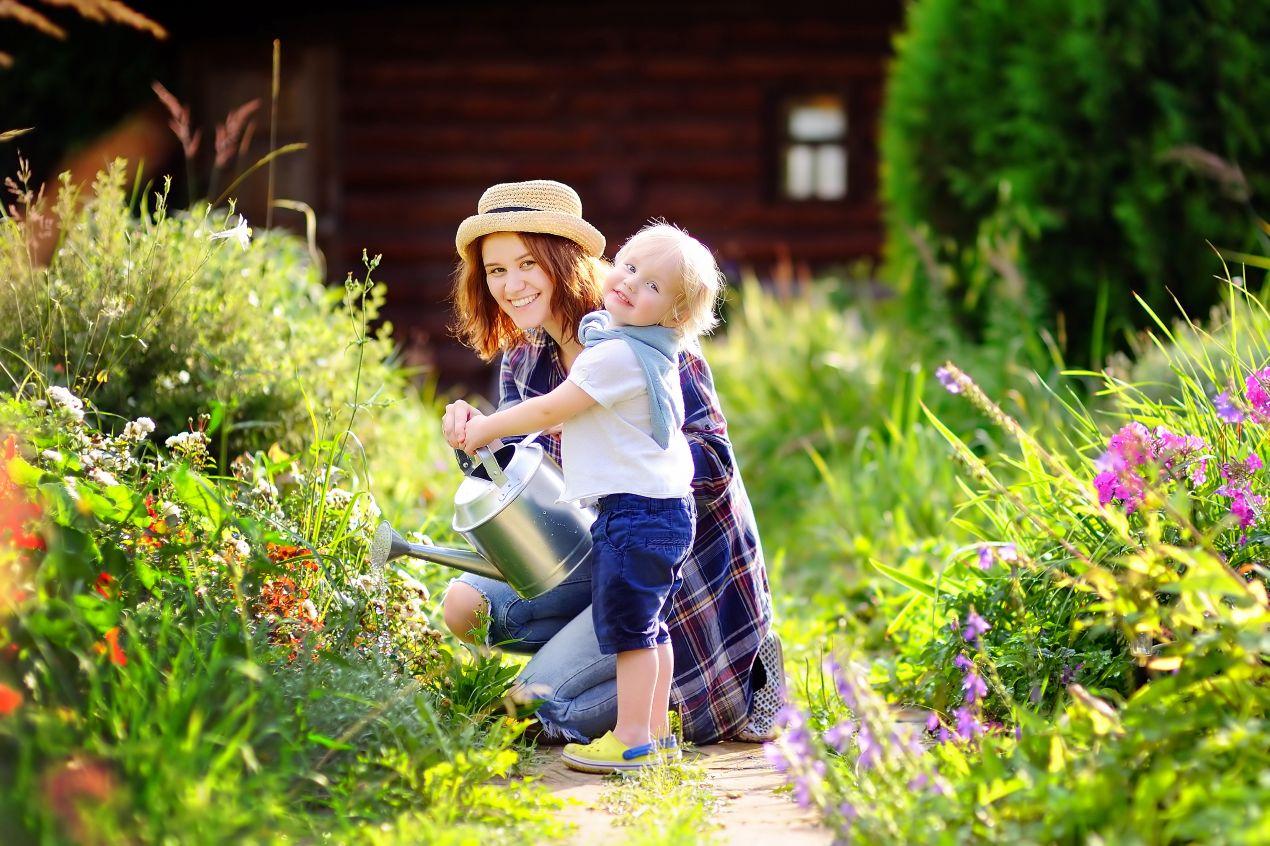 Mutter und Kind giessen gemeinsam Blumen in einem naturnah gestalteten Garten mit umweltfreundlichen Pflanzgefaessen