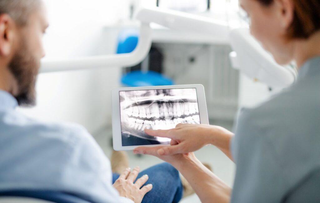Zahnarzt erklaert einem Patienten digitales Roentgenbild auf Tablet in einer spezialisierten Praxis fuer oralchirurgie essen