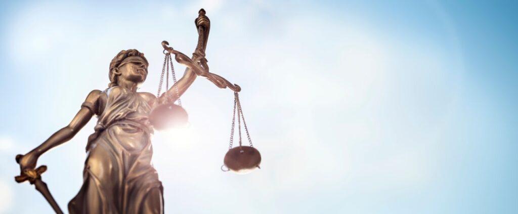 Rechtsanwalt Potsdam Strafrecht: Bronze-Statue der Justitia mit Waage und Schwert vor blauem Himmel als Zeichen fuer objektive Strafverteidigung