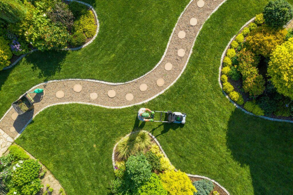 Professionelle Gartenpflege mit Rasenmäher und Kiesweg in gepflegter Anlage