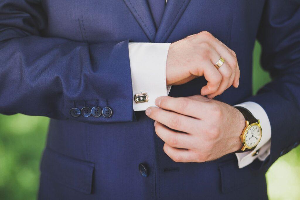Detailaufnahme eines Mannes im blauen Anzug mit goldfarbenem Ehering am Finger und Uhr am Handgelenk