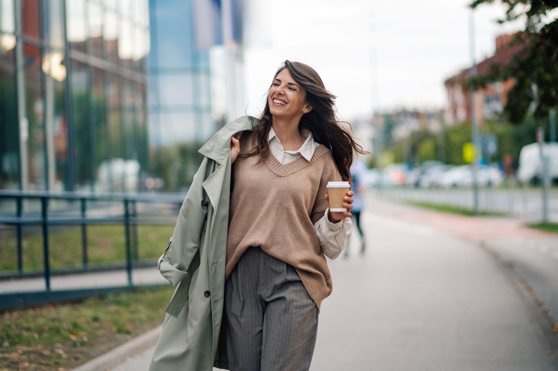 Frau mit langen Haaren und Coffee-to-go auf dem Weg ins Büro – Tape In Extensions sorgen für alltagstauglichen Look